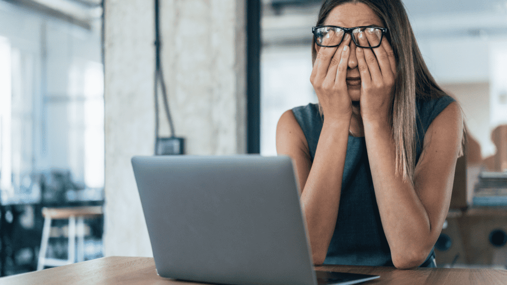 A woman feeling busy and overwhelmed at her laptop.